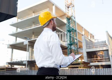 Man Controlling Building. Builder making marks in Clipboard. House Building Stock Photo