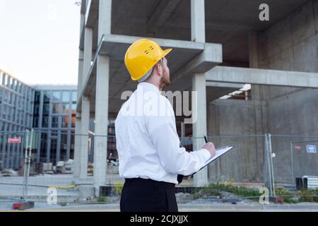 Man Controlling Building. Builder making marks in Clipboard. House Building. Businessman Stock Photo