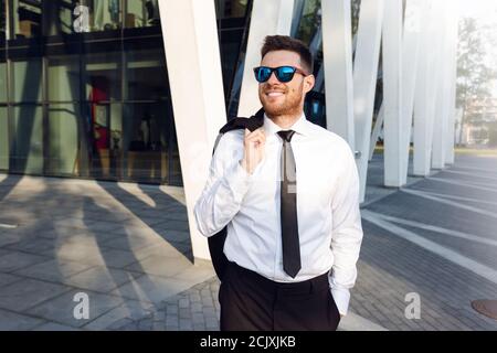Businessman Walking on Sunny day with jacket on his Shoulder. Business man Smiling with Sun Glasses Stock Photo