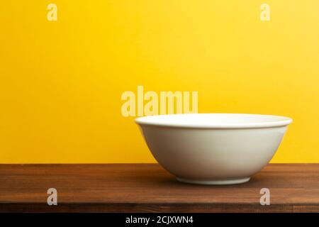 White ceramic bowl on a yellow colored background. Empty plate for salad or soup on wooden table Stock Photo