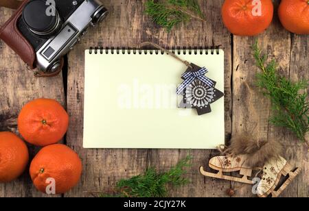 Tangerines, coniferous branches, wooden Christmas tree and skates, Notepad and retro camera on a natural wooden background. Stock Photo