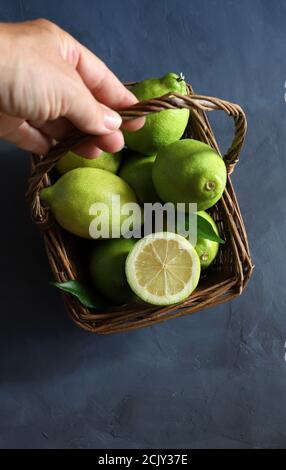 Hand holds a wicker basket with fresh lemons on grey background. Top view. Selective focus. Copy space. Stock Photo