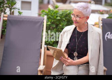 a beautiful elderly lady is chatting online with a friend in the park Stock Photo