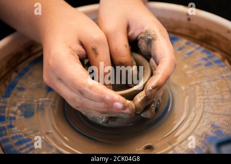 Child hands shaping a pot on a turning ceramic pottery wheel. Stock Photo
