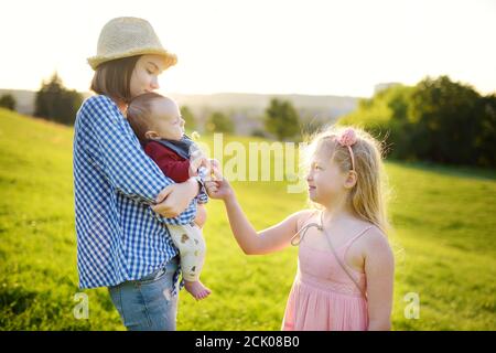 Two big sisters admiring their adorable infant brother. Two young girls holding their new baby boy sibling. Kids with large age gap. Big age differenc Stock Photo