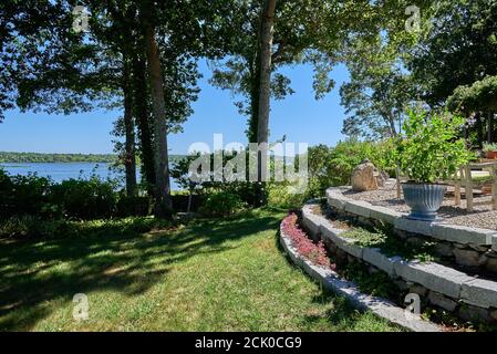 Sunny summer garden and patio with granite steps by a river. Stock Photo