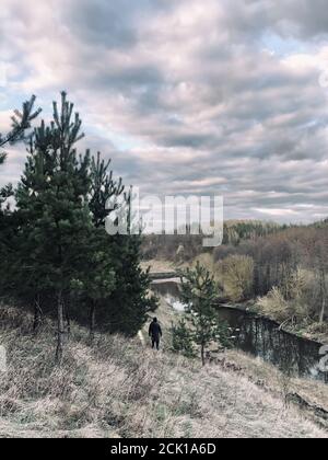 A young man stands in a jacket and a hood on a hill above the river Stock Photo