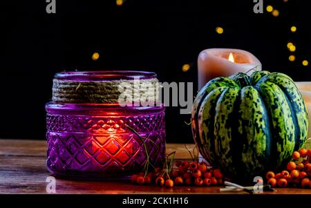 Purple lantern, green pumpkin rowan berries and candle on wooden rustic table and black background with yellow bokeh dots, autumnal warm mood in cozy Stock Photo
