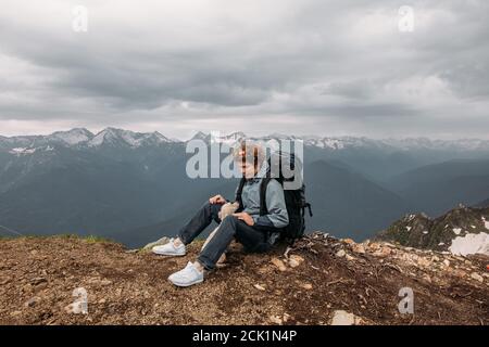 young man in sporty clothes with rucksack is talking with his dog while resting on the mountain Stock Photo
