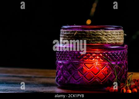 Purple lantern, orange golden nugget pumpkin rowan berries and two candles on wooden rustic table and black background with yellow bokeh dots Stock Photo