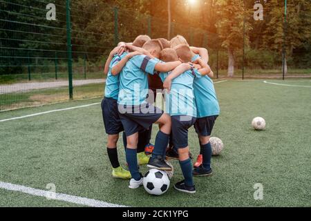 Children soccer team and coach hugs each other on football field before match Stock Photo
