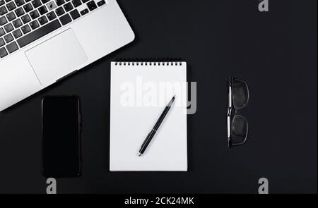 Black office desk with laptop, smartphone, pen and glasses  Stock Photo