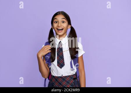 Excited amazed indian school girl holds backpack isolated on violet background. Stock Photo