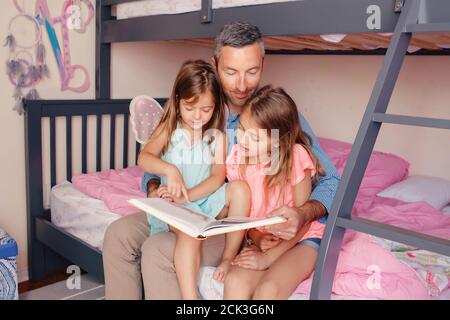 Home education homeschooling. Dad reading book to daughters girls in bedroom. Family father and children at home spending time together. Fathers day Stock Photo