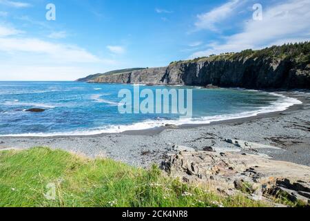 Bright blue ocean with a small white wave as it meets the empty pebbled beach in the summer. Stock Photo