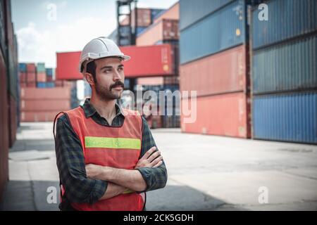 Portrait of Confident Transport Engineer Man in Safety Equipment Standing in Container Ship Yard. Transportation Engineering Management and Containers Stock Photo