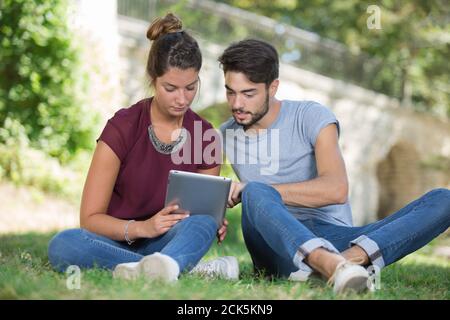smiling young couple talking and using tablet outdoors Stock Photo