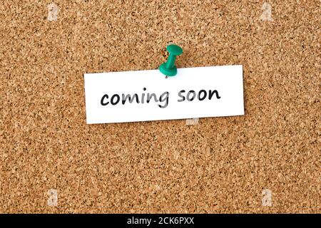 Coming soon. Text written on a piece of paper or note, cork board background. Stock Photo