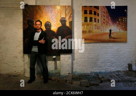 Street artist James Cochran, also known as Jimmy C, poses next to his spray painted pictures 'Riot Police' (L) and  'Defy part 3' at the Pure Evil Gallery in London October 10, 2013. The paintings were originally inspired by the London riots in 2011. REUTERS/Stefan Wermuth (BRITAIN - Tags: ENTERTAINMENT SOCIETY)