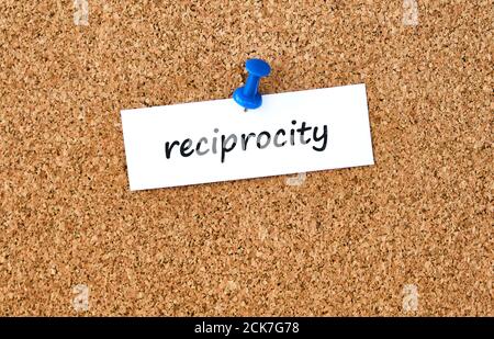 Reciprocity. Word written on a piece of paper or note, cork board background. Stock Photo