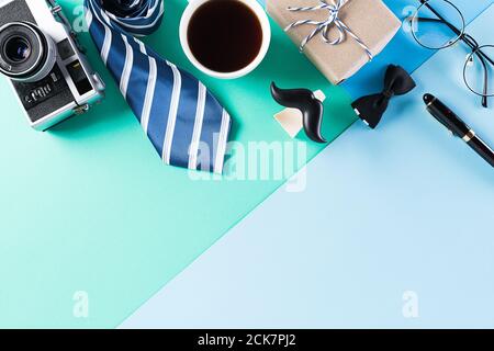 Happy Fathers Day background concept with coffee cup, decorated bowtie, necktie, eyeglasses, gift box and mustache on bright pastel background. Stock Photo