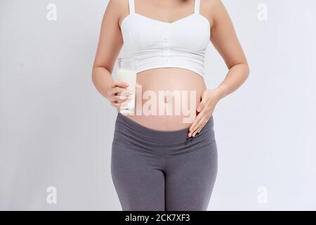 Happy pregnant woman drinking a glass of fresh milk and touching her belly Stock Photo