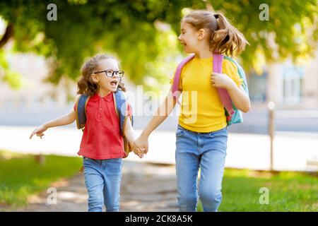 Pupils of primary school. Girls with backpacks outdoors. Beginning of lessons. First day of fall. Stock Photo