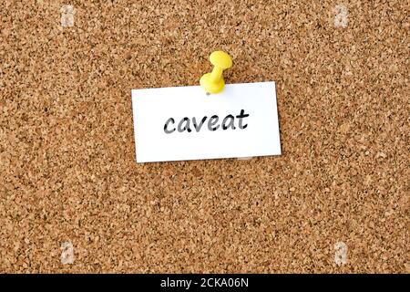 Caveat. Word written on a piece of paper or note, cork board background. Stock Photo