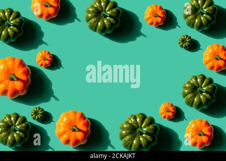 Pumpkins pattern frame on turquoise background, top view. Orange and green pumpkins with hard shadows, halloween or autumn concept. Copy space. Stock Photo
