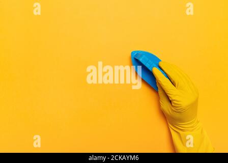 blue brush for washing clothes in a hand in rubber yellow gloves on a yellow background. place for text. Stock Photo