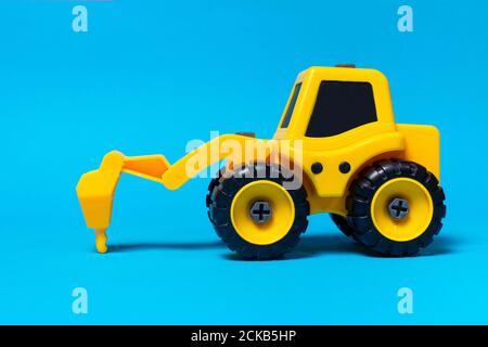 Children's toy yellow tractor truck drill on a blue background. Plastic construction equipment, toy store Stock Photo