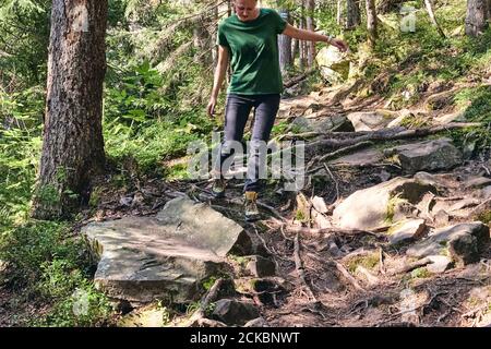 Close-up Legs In sport trekking shoes on green grass and rocky stones with moss of mountain autumn forest. Woman climbs in sporty clothes and backpack Stock Photo