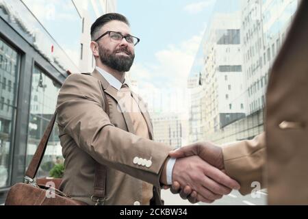 Mature bearded man in eyeglasses greeting his colleague outdoors Stock Photo