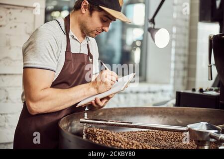Handsome man taking notes while using coffee roasting machine Stock Photo