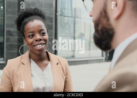 African young woman talking to man and smiling while they standing on the street in the city Stock Photo