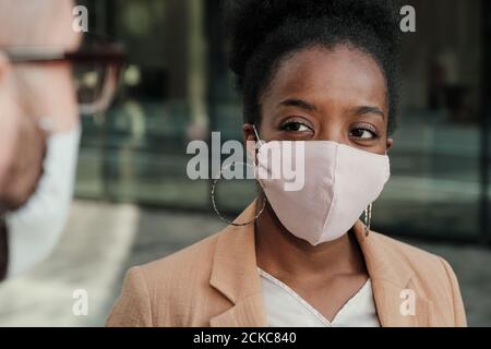 African young woman in protective mask talking to man while they standing outdoors Stock Photo