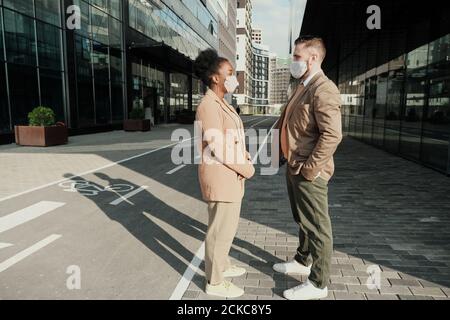 Two business colleagues wearing protective masks talking to each other they have meeting in the city Stock Photo