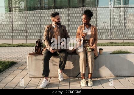 Two business colleagues sitting on bench and talking to each other outdoors Stock Photo