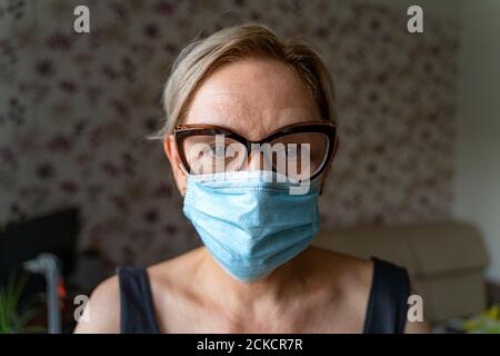 Caucasian woman with medical mask at home. Loneliness, mental health in quarantine. Middle aged mature people Stock Photo