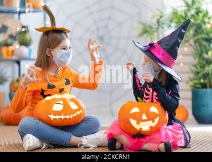 Cute little children girls in carnival costumes wearing face masks. Happy family preparing for Halloween protecting from COVID-19. Stock Photo