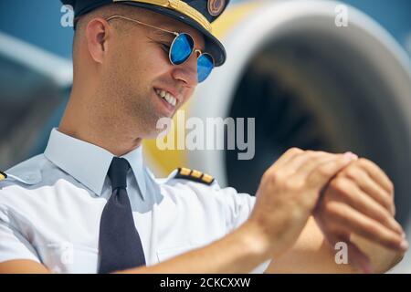 Cheerful male pilot looking at wristwatch at airfield Stock Photo