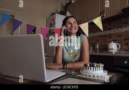Asian woman virtual happy hour meeting birthday party with cake online, listens to birthday greetings on her cell phone. Stock Photo