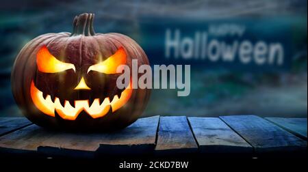 One spooky halloween pumpkin, Jack O Lantern, with an evil face and eyes on a wooden bench, table with a misty night background with space for product Stock Photo
