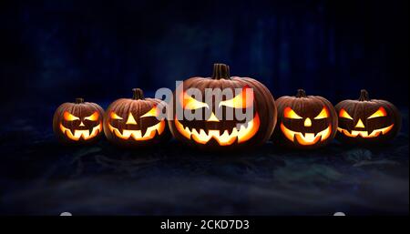 Five spooky halloween pumpkin, Jack O Lantern, with an evil face and eyes on the forest floor at night with a dark background. Stock Photo