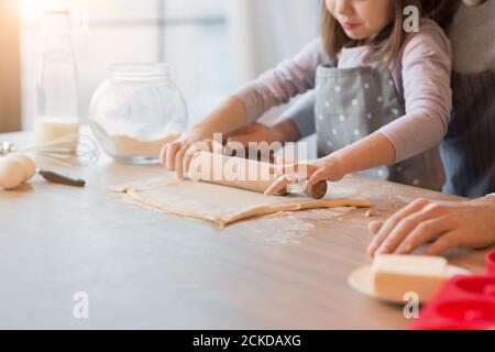 Father and daughter rolling dough together in kitchen to make cookies, cropped Stock Photo