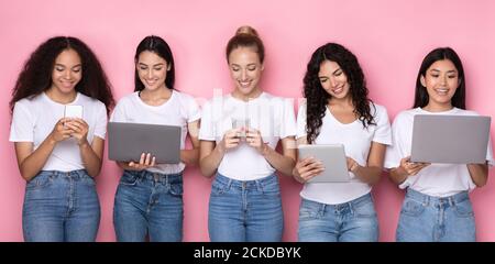 Multiracial Young Women Using Gadgets, Computers And Smartphones, Pink Background Stock Photo