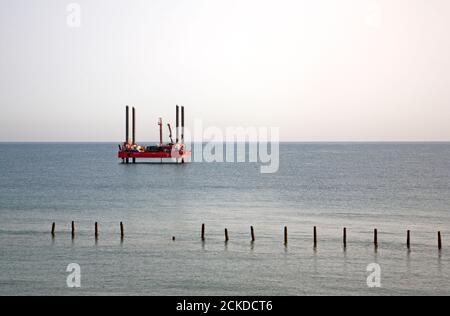 A small jack-up rig positioned close to shore with old sea defence timbers in the foreground at Happisburgh, Norfolk, England, United Kingdom. Stock Photo