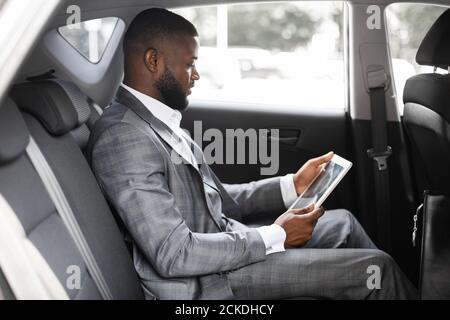Concentrated black guy manager using digital tablet in car Stock Photo