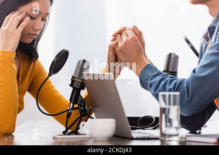 broadcaster holding hand of upset asian woman touching head during interview Stock Photo