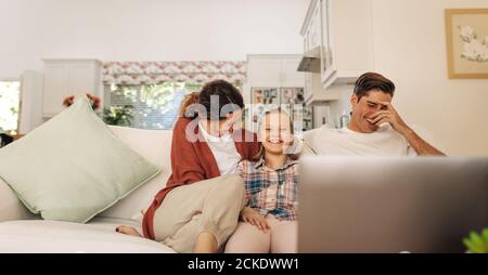 Girl with her parents smiling together on the sofa. Happy family of three having a great time together at home. Stock Photo
